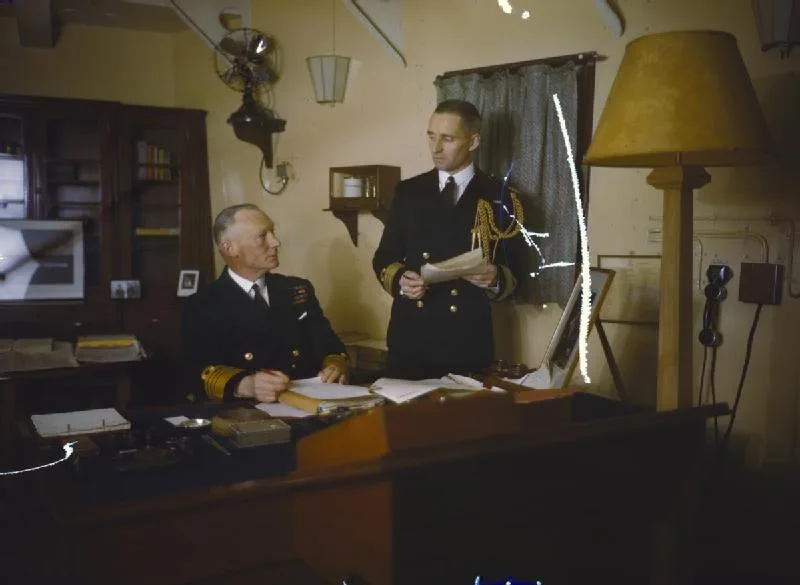 A scratched 1942 photo of two naval officers in a ship's office, murky color