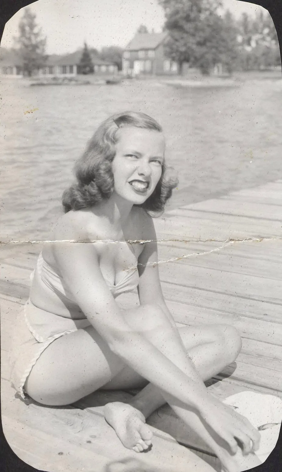 A 1945 snapshot of a woman on a dock with a hard crease line across the middle.