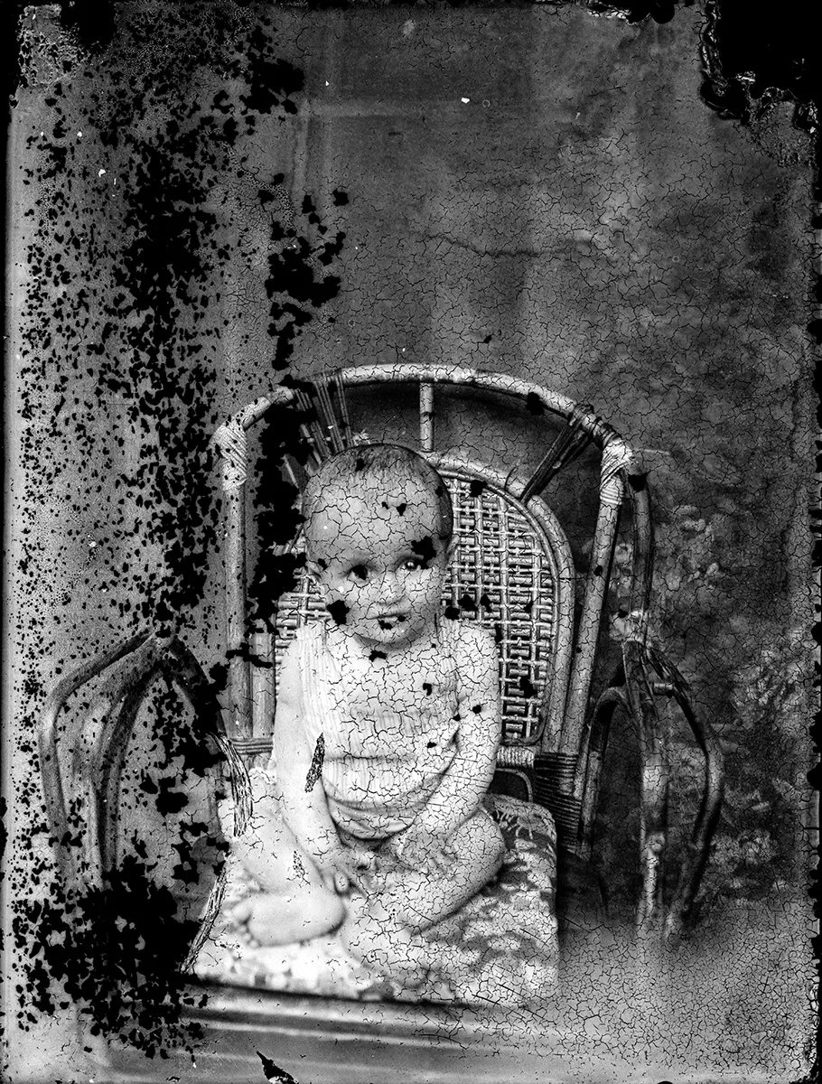 A 1930s glass plate photo of a child covered in mold blotches and cracked emulsion.